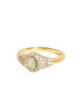Gold ring with a green gemstone and diamond accents on a beige background