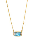 Gold necklace with a blue gemstone pendant on a light beige background