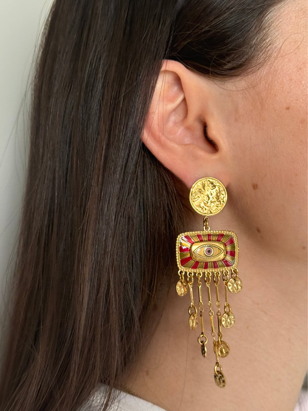 Close-up of a person wearing a gold and red earring with dangling elements.