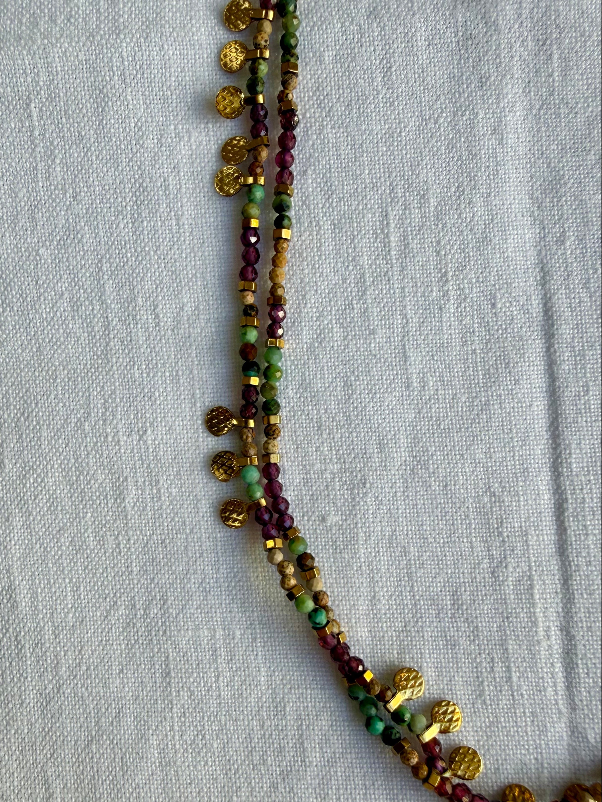 Beaded necklace with gold and multicolored beads on a light gray fabric background