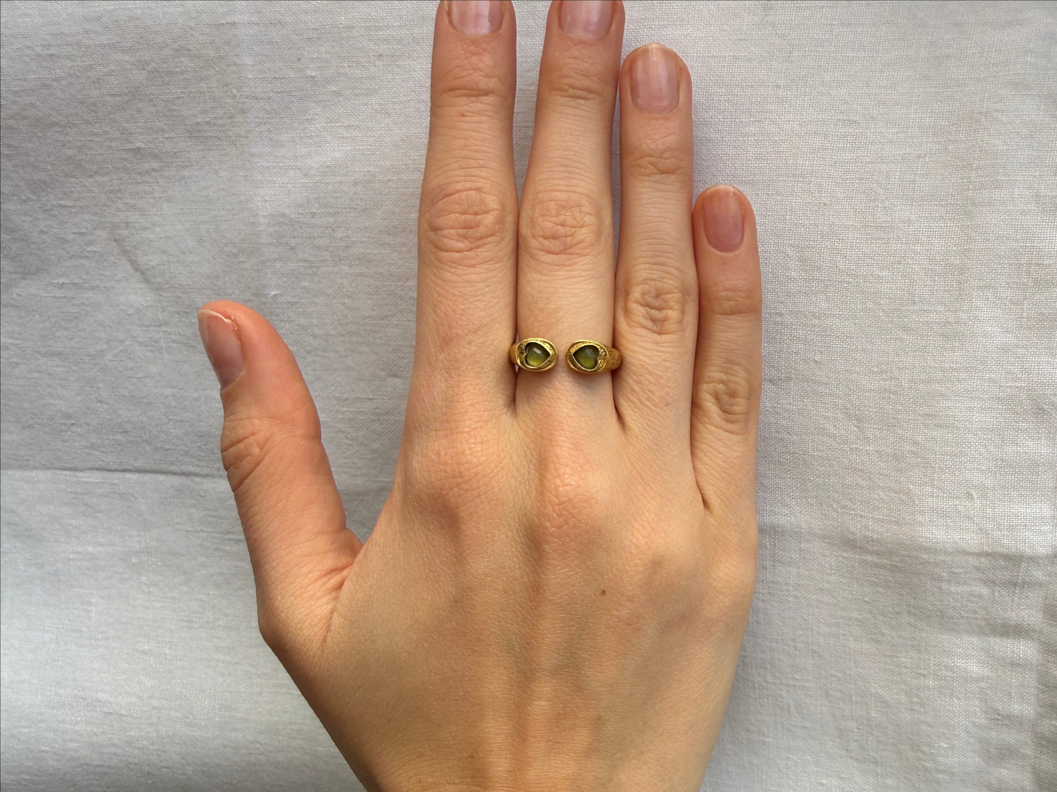 Hand wearing a gold ring with green gemstones on a light gray background