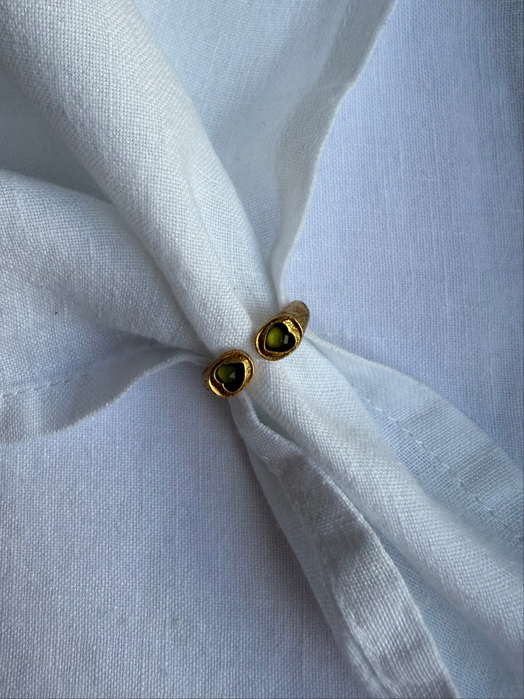 Gold earrings with green gemstones on a white fabric background
