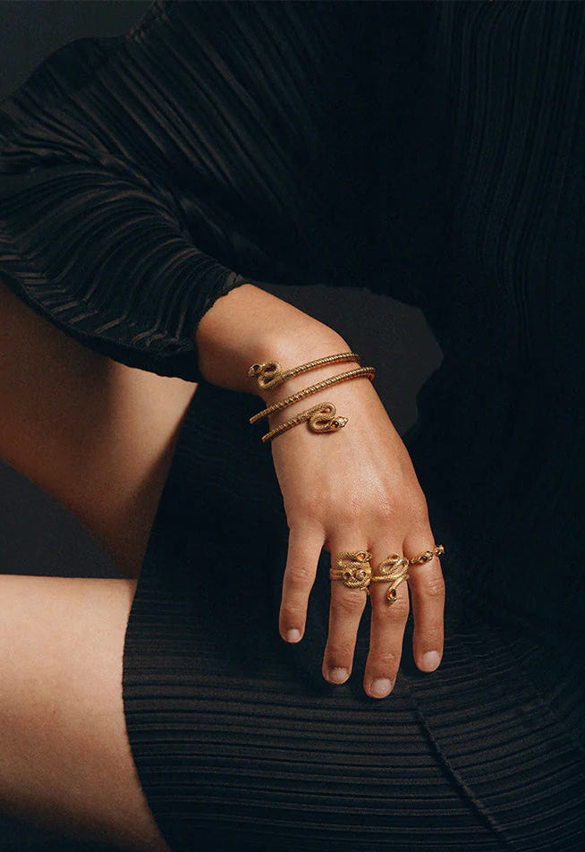 Hand wearing gold bracelets and rings on a dark background
